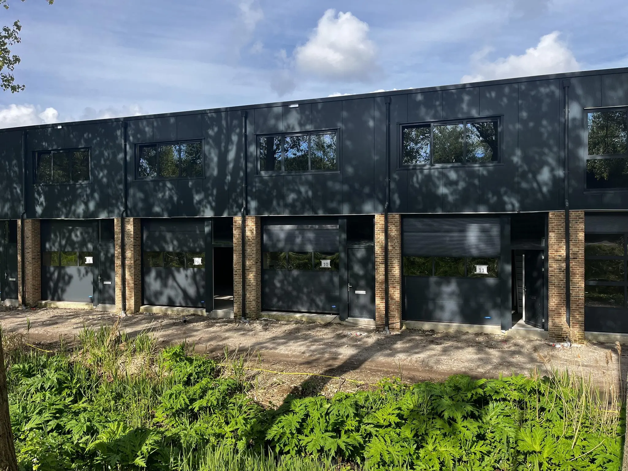 Bedrijfsverzamelgebouw aan de Broekdijk West met meerdere zwarte units en overheaddeuren onder een zonnige hemel.